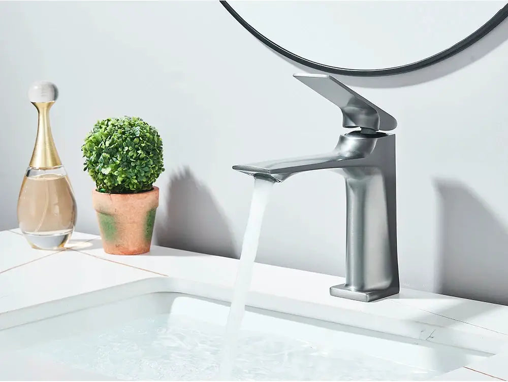 Deck-mounted bathroom faucet with a single lever in chrome finish, water flowing into a white sink