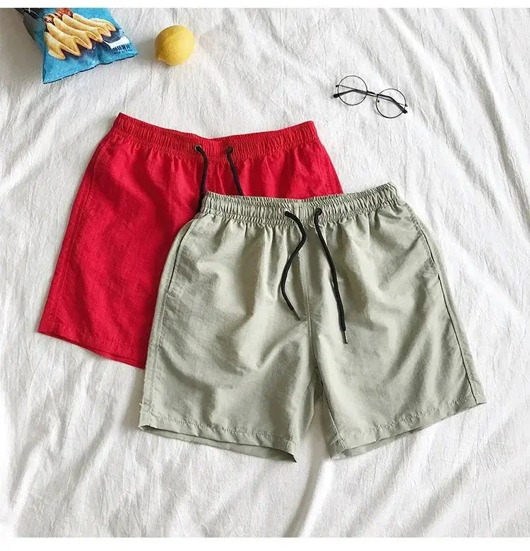 Simples Market two pairs of men's swim shorts: red and light gray board shorts with drawstring waists.