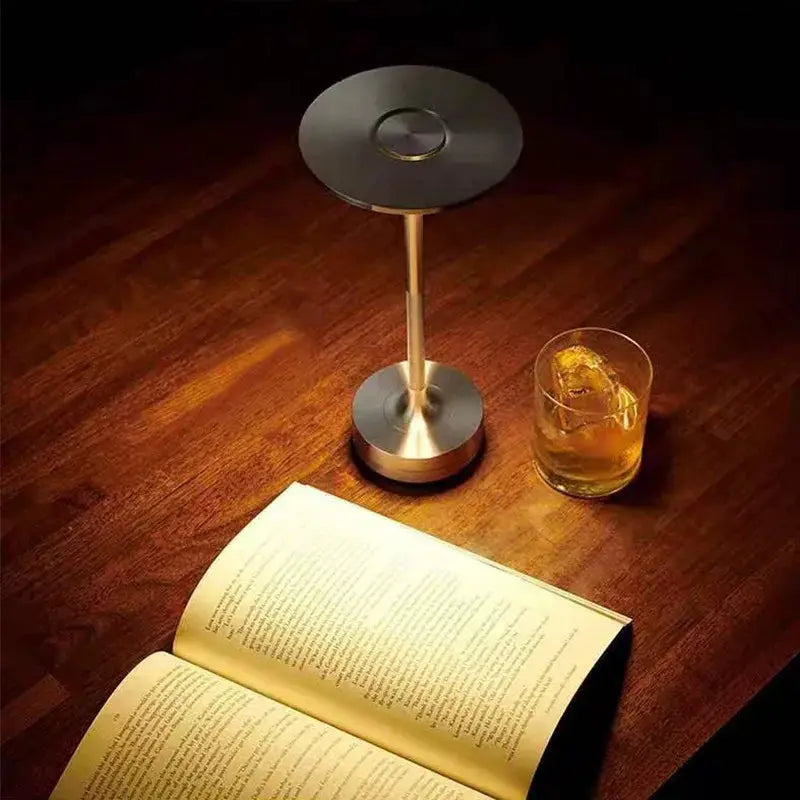 Table lamp with brass-tone stem and round black head on a metal base; wireless rechargeable decorative lamp.