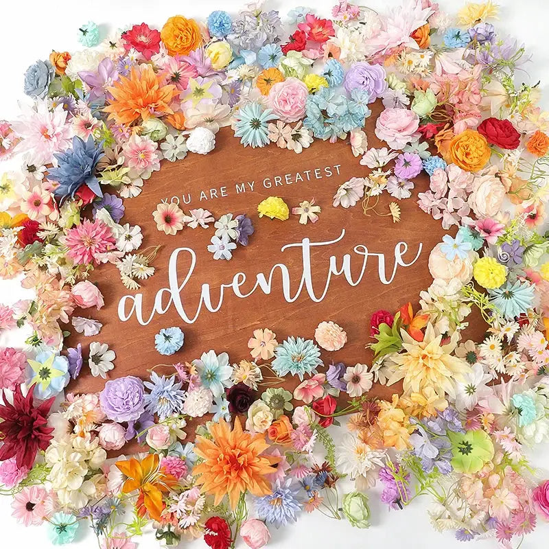 Silk artificial flowers mix in bright colors arranged around a wooden sign with adventure text, Simples Market