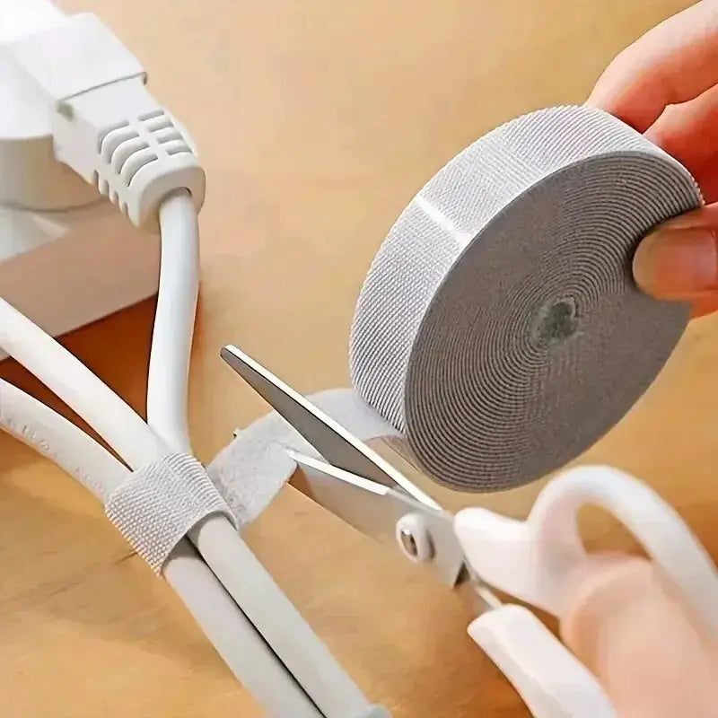 Cable organizer tape in gray fabric being wrapped around earphones and power cables with scissors.