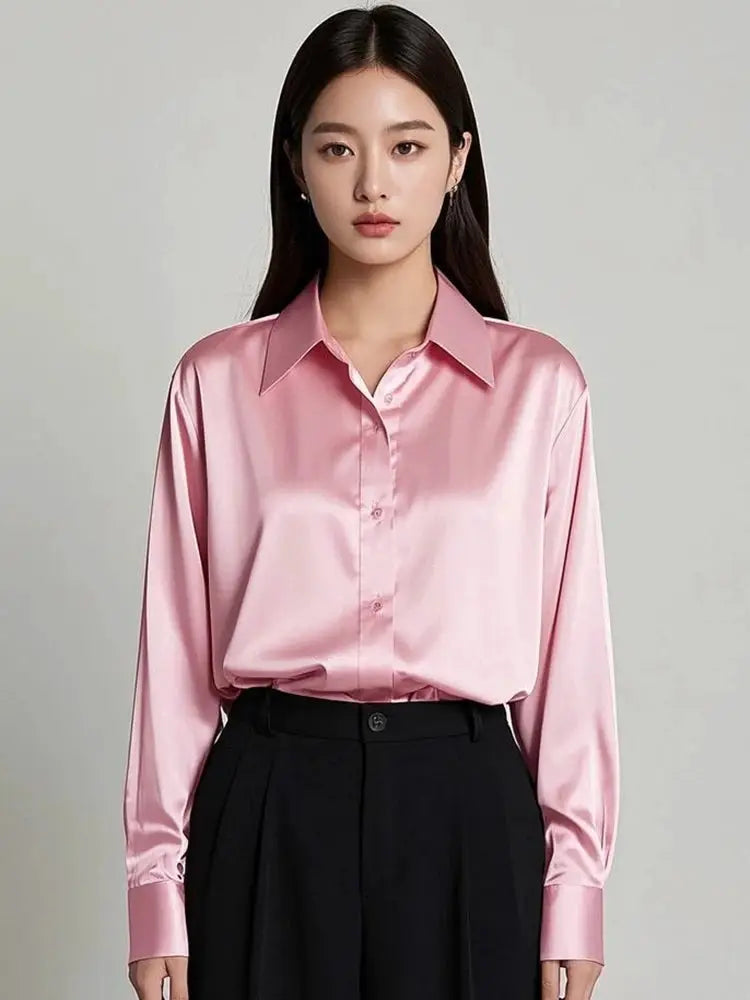 Pink satin blouse with a pointed collar and long sleeves, tucked into black tailored trousers.