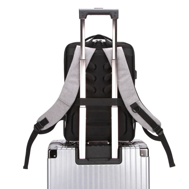 Men's anti-theft hard-shell backpack, black with gray straps, atop a silver suitcase