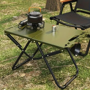 Portable folding camping table by Simples Market with olive-green top and black frame, featuring kettle, pot, and mug.
