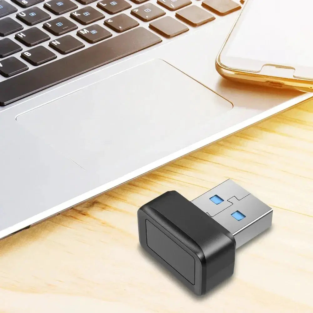 USB fingerprint key reader with black housing and USB-A plug beside a laptop.