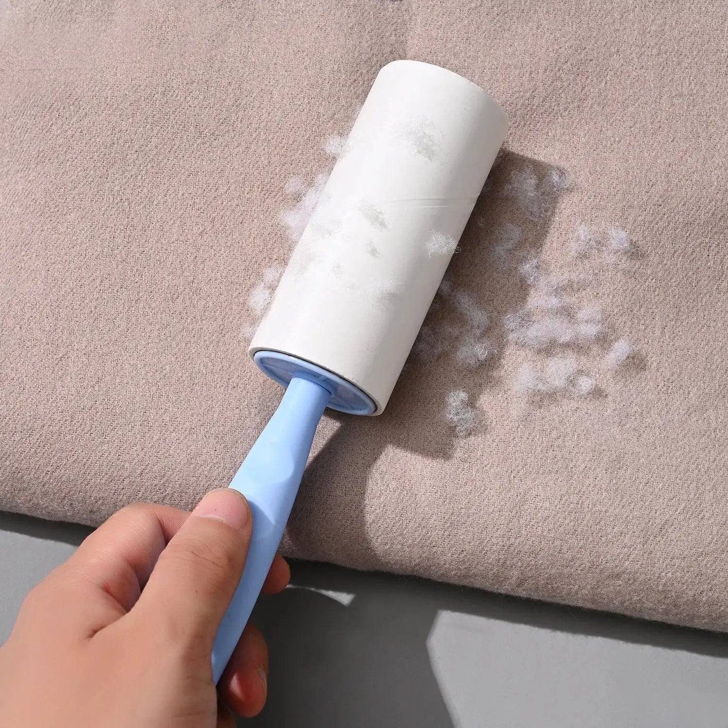 Lint roller with blue handle and white sticky roller removing pet hair from beige upholstery.
