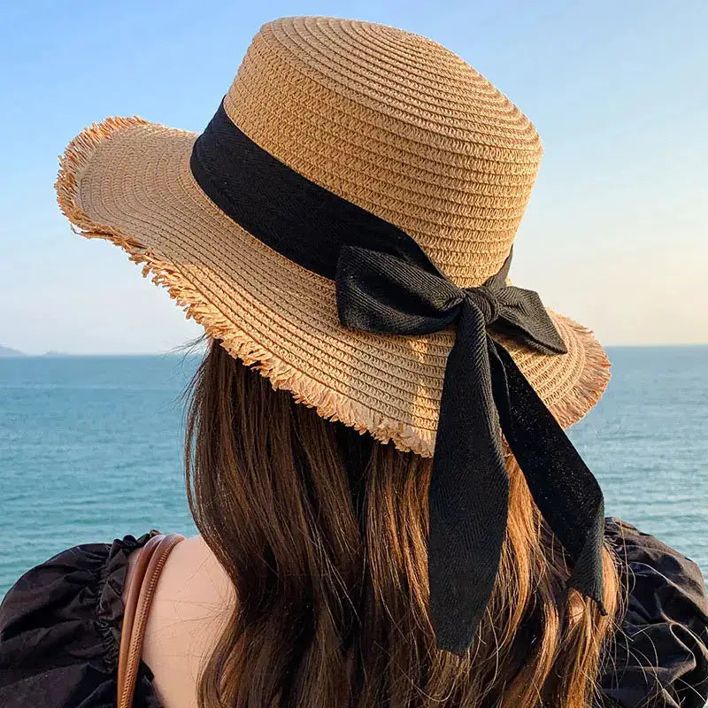 Beige straw sun hat for women with wide brim and black ribbon bow by Simples Market
