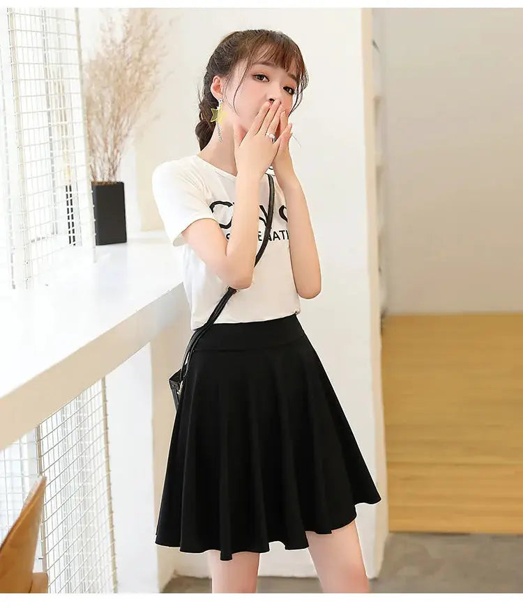 Flared black pleated mini skirt with a crossbody bag worn by a model in a white tee