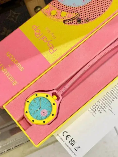 Swatch watch with yellow bezel, turquoise dial, pink strap in bright pink packaging.