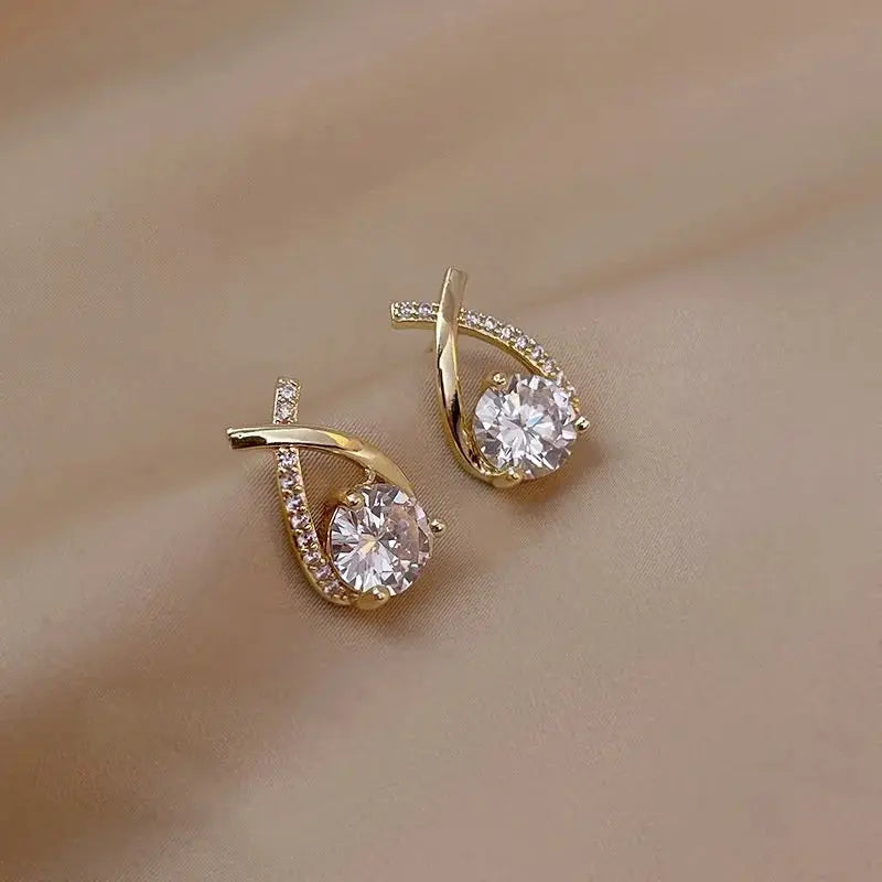 SKEDS cross fishtail earrings pair by Simples Market; gold-tone with clear crystal stones.