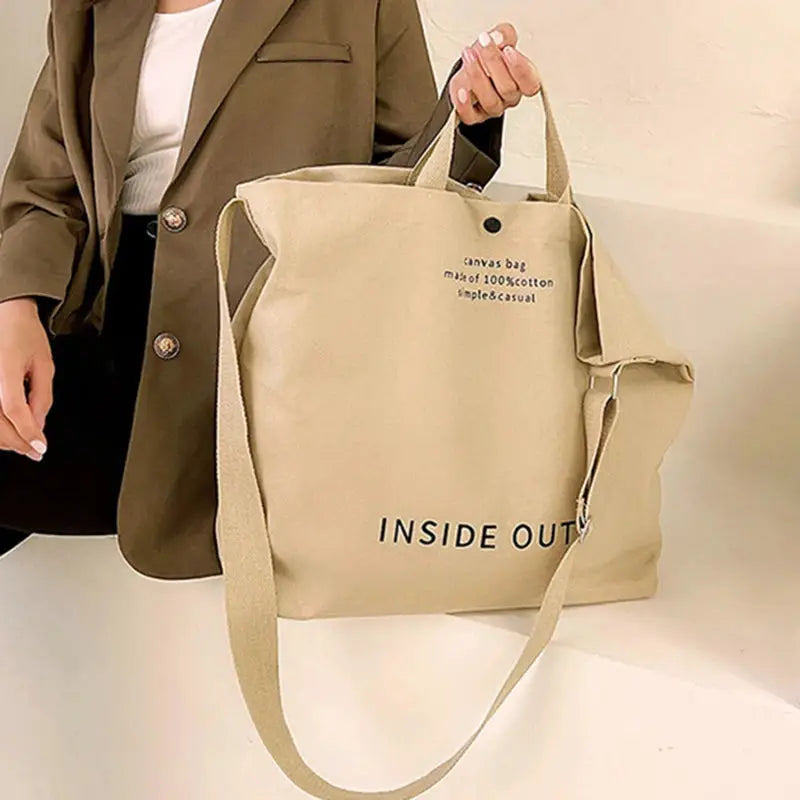 Beige canvas crossbody bag with long strap and top handles; large-capacity casual tote with INSIDE OUT print