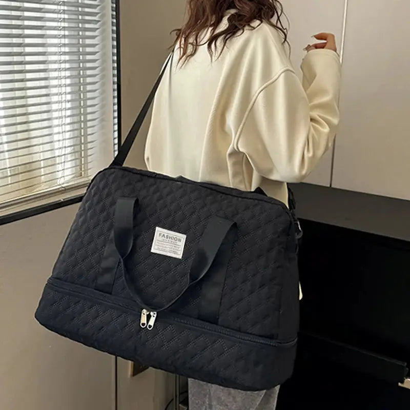 Black quilted duffle bag with two top handles and shoulder strap, front zip pocket, FASHION label