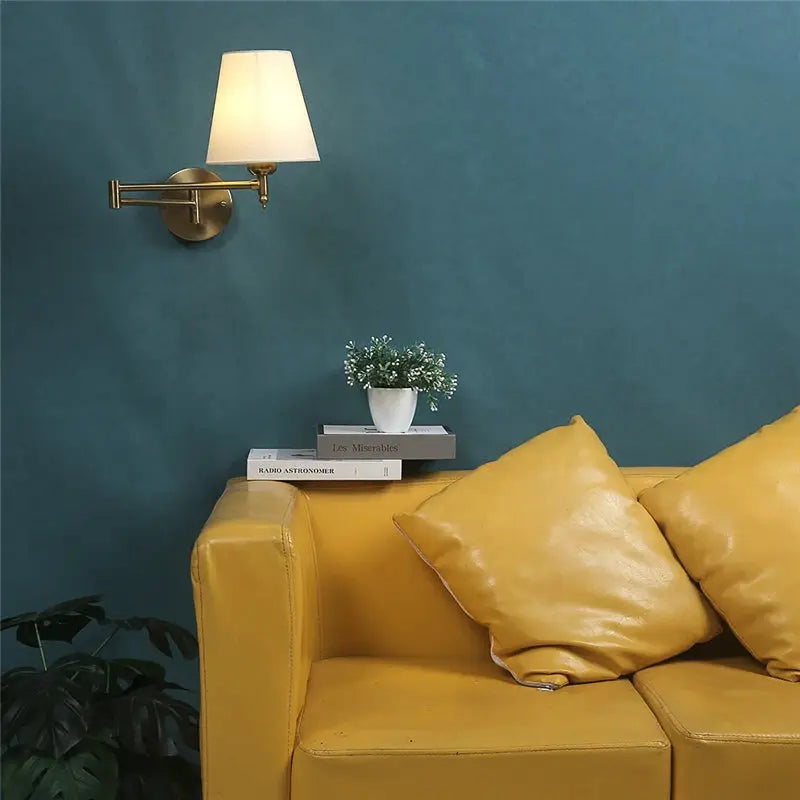 Nordic adjustable folding wall lamp with brass finish and white shade mounted on teal wall above yellow sofa