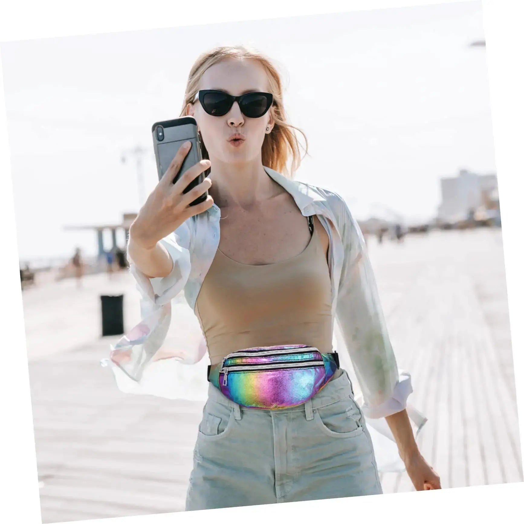 Holographic fanny pack waist bag in rainbow metallic finish, worn around the waist by a woman at the beach