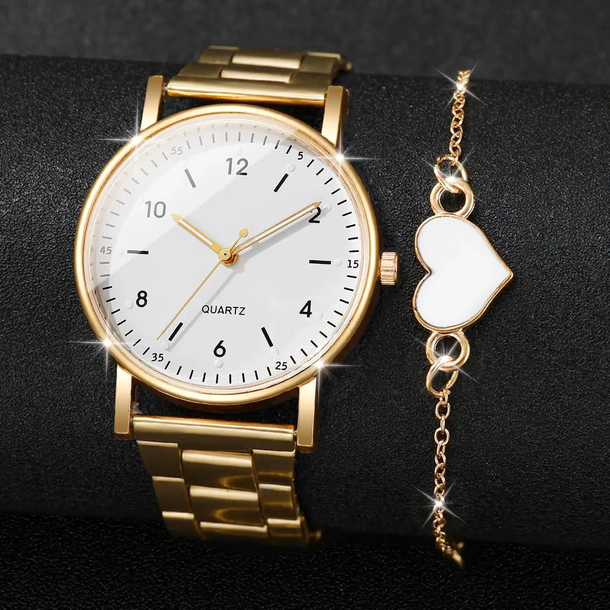 Gold-tone women's quartz wristwatch with white dial and Arabic numerals, paired with a heart charm bracelet in a 2–4 piece set.