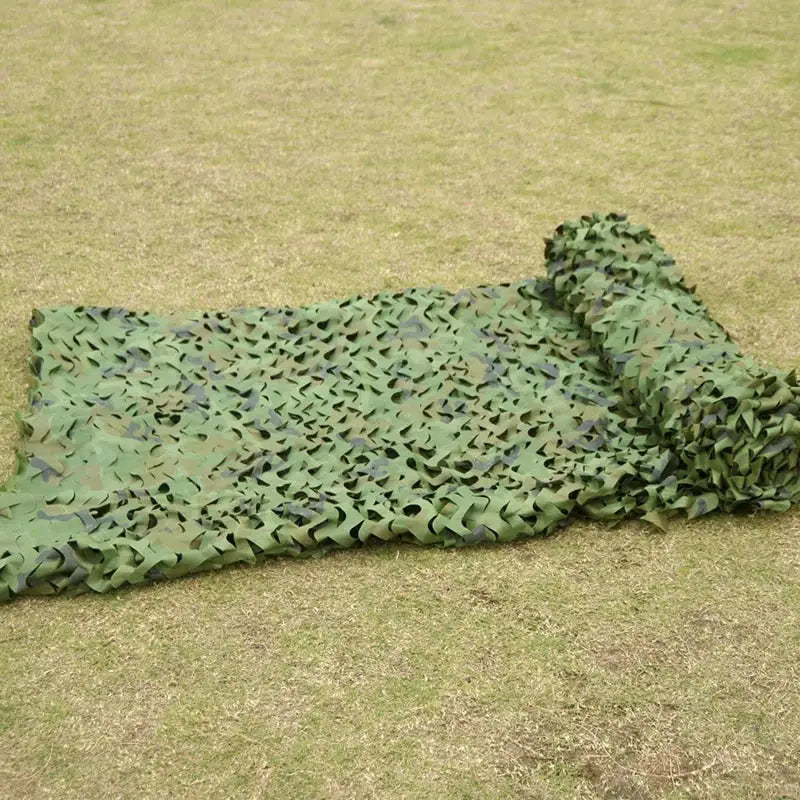 Military camouflage netting in green camouflage pattern laid out on grass with rolled edge
