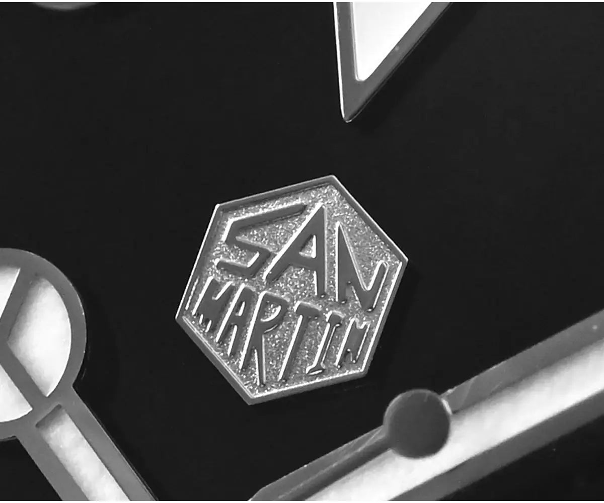 San Martin hexagonal metal logo badge on black surface with watch parts