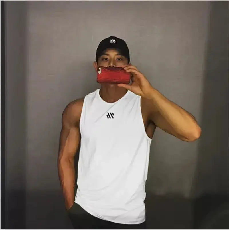 Men's white sleeveless bodybuilding tank top by Simples Market with small black logo, model taking a mirror selfie.