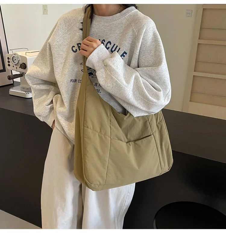 Trendy beige soft-cloth shoulder bag, solid color crossbody worn by a woman in a gray sweatshirt.