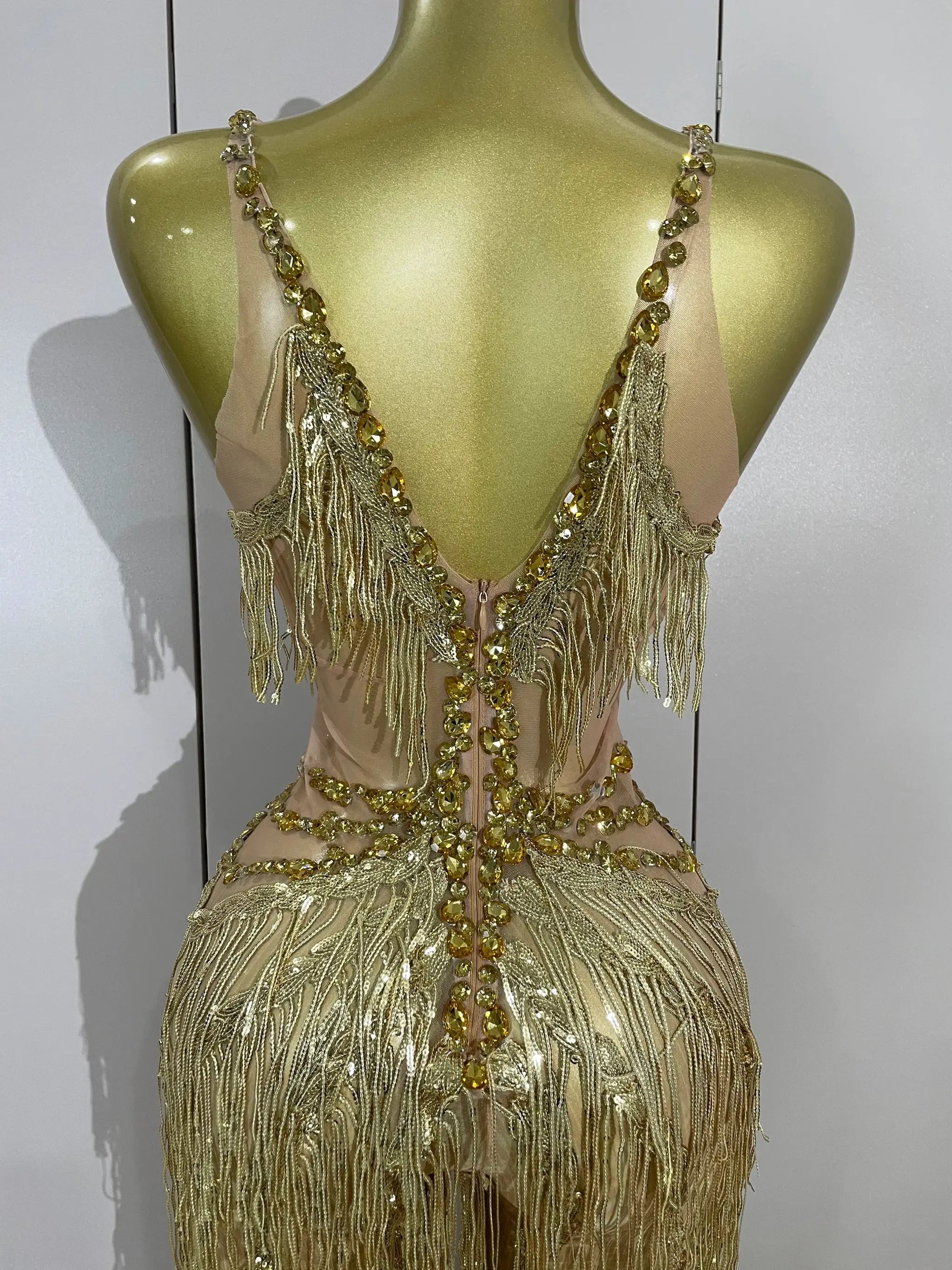 Jumpsuit with gold rhinestones and fringe on nude fabric for stage performance.