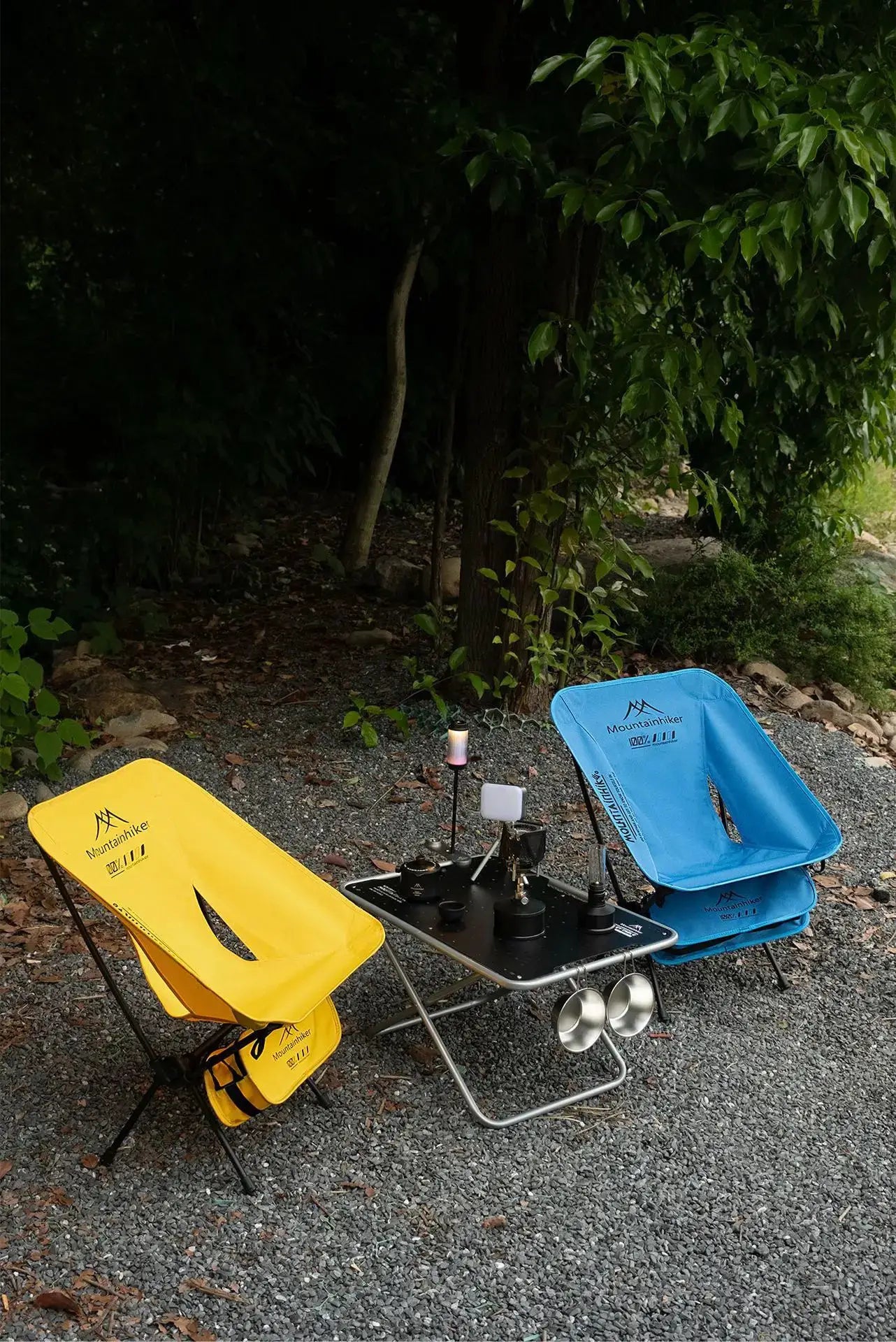 Foldable Moon chairs set in yellow and blue with Mountainhiker logos, outdoors beside a small camping table