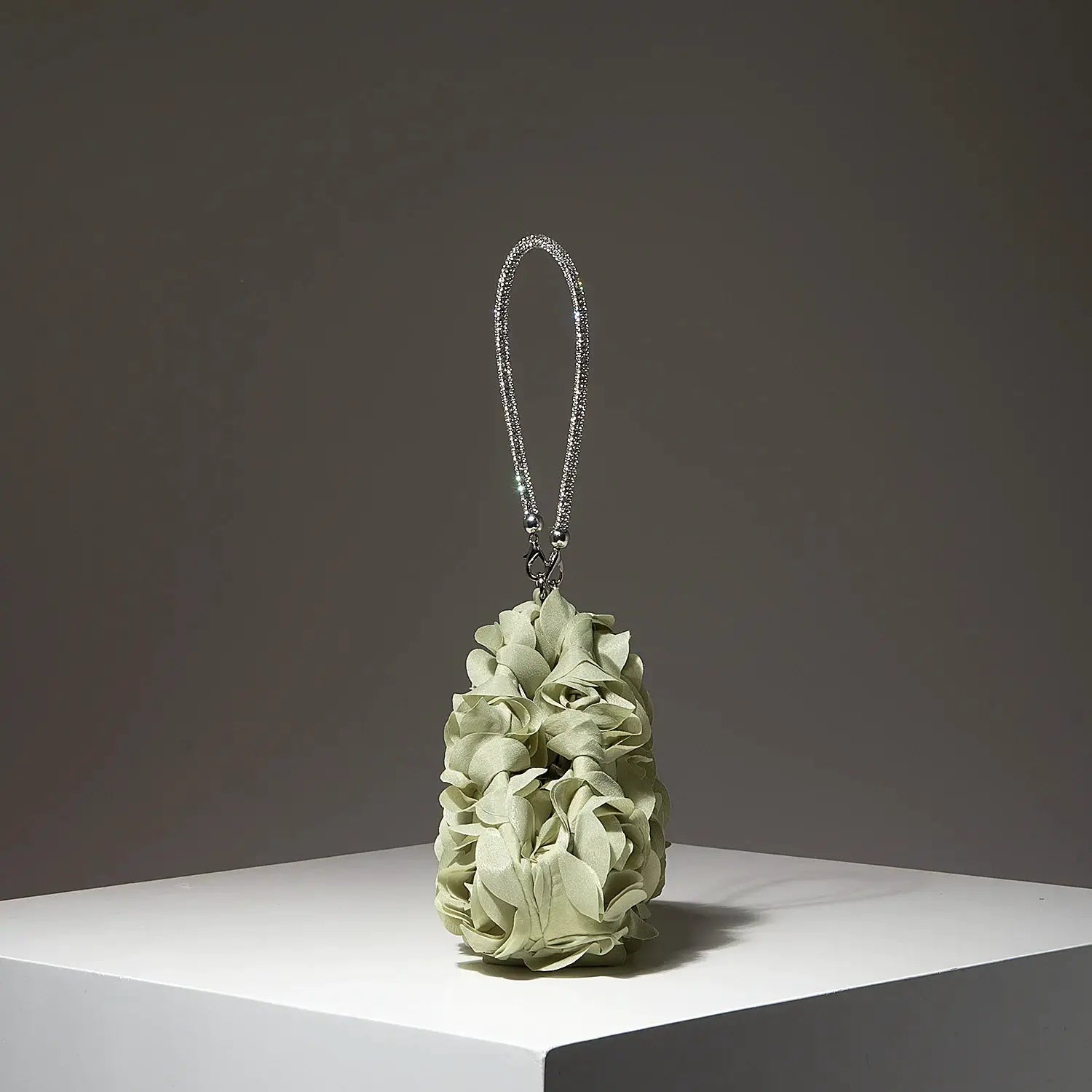 Mini bridal purse with crystal-embellished silver strap, perched on pale green fabric flower bouquet.