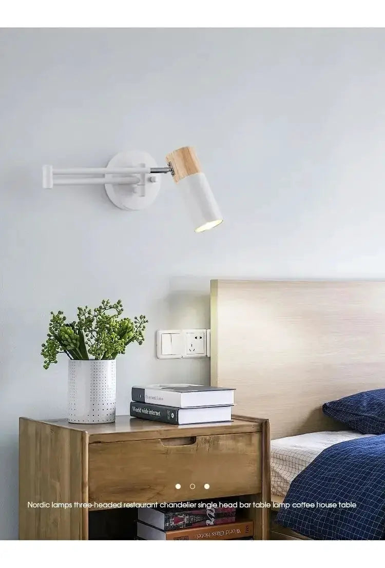 Wall-mounted reading lamp with white body and wood accent, adjustable arm over a wooden bedside table.