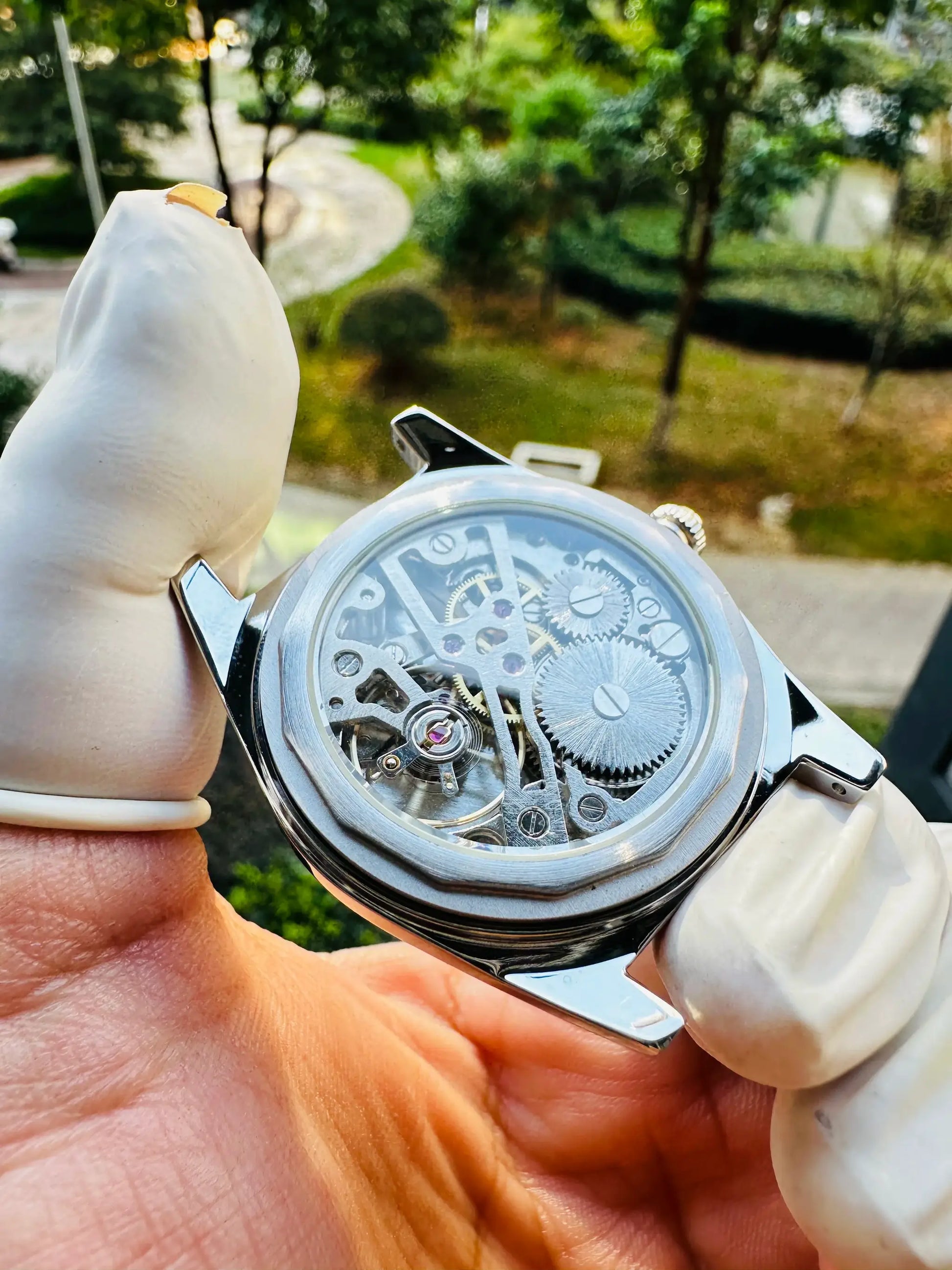 Mens skeleton mechanical watch with visible gears in a silver 36mm case, held by gloved hand.