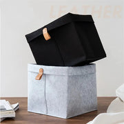 Two gray and black felt storage baskets with tan leather handles for home organization