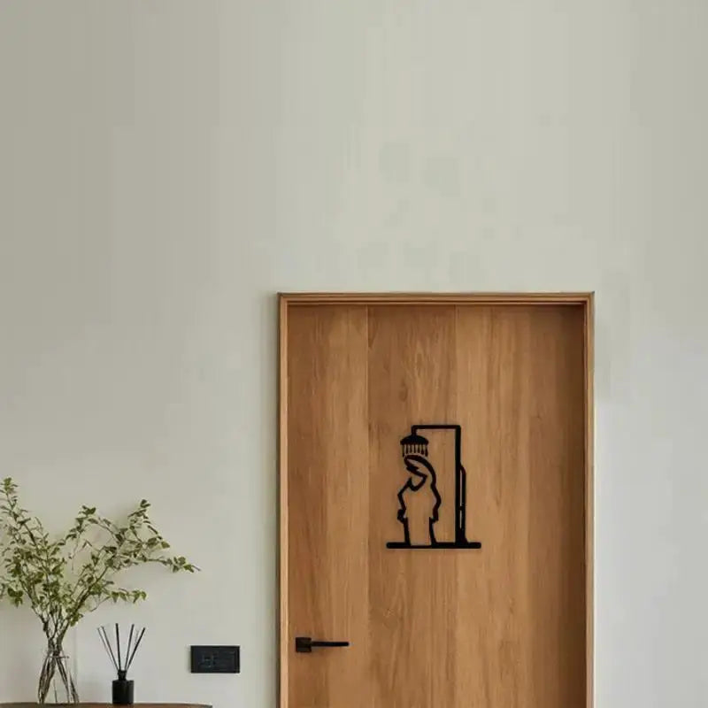 Black shower-figure metal wall art on a wooden door, minimalist bathroom decor sign