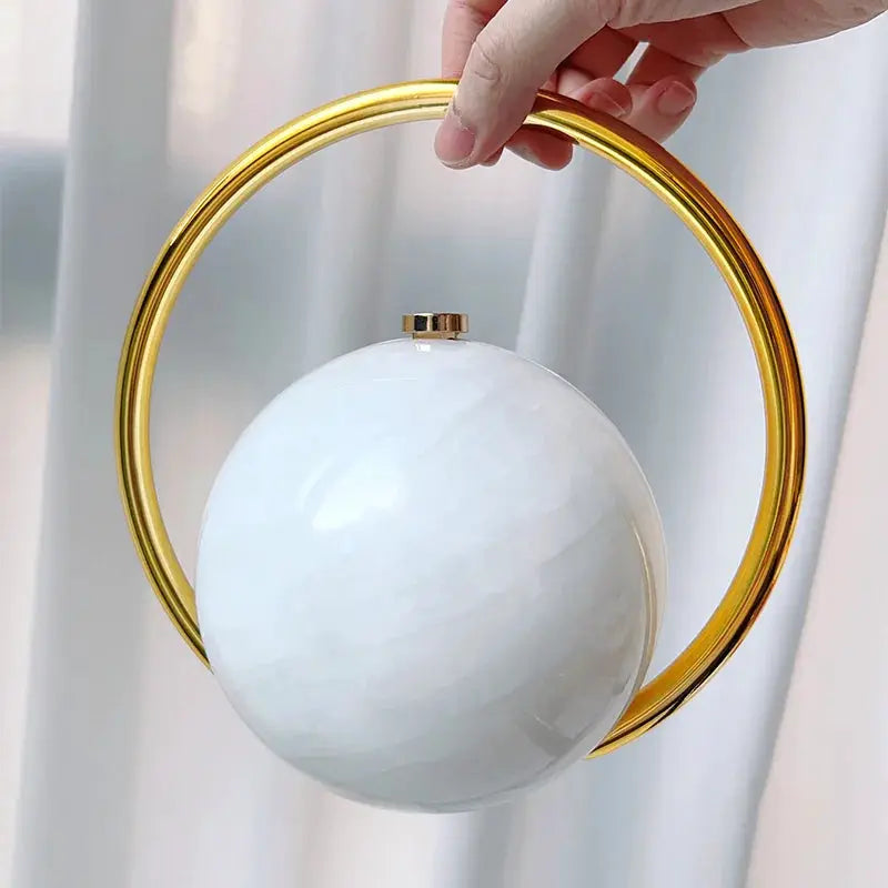 Luxury evening clutch by Simples Market: white acrylic spherical handbag with gold hoop handle.