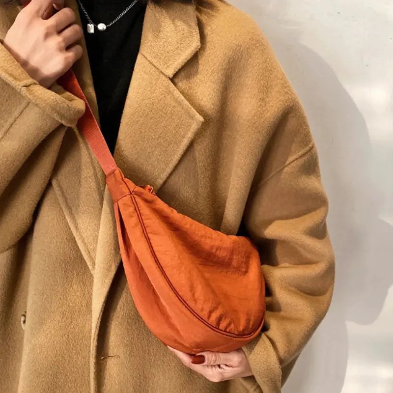 Casual orange nylon hobo crossbody bag for women, worn with a camel coat.
