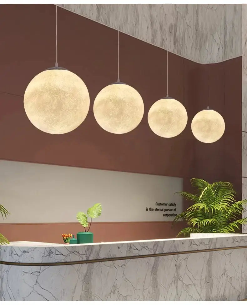 Nordic Moon LED pendant lights; four warm-glow globe lamps in varying sizes hanging over a marble counter.