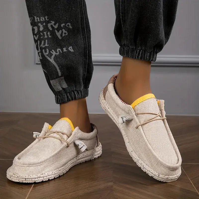 Pair of men's beige canvas loafers with yellow heel trim; breathable casual driving/walking shoes with a textured sole.