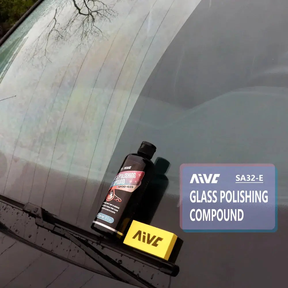 AIVE glass polishing compound bottle with a yellow sponge applicator resting on a car windshield during detailing