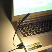Portable USB book light by Simples Market with flexible neck, black mini LED lamp connected to a laptop.