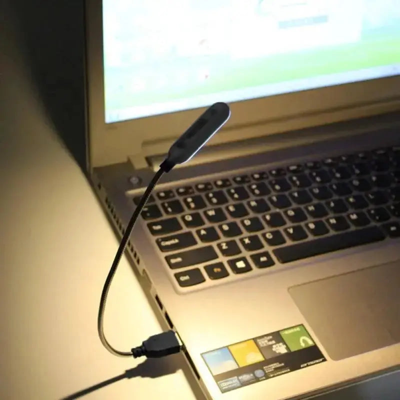 Portable USB book light by Simples Market with flexible neck, black mini LED lamp connected to a laptop.