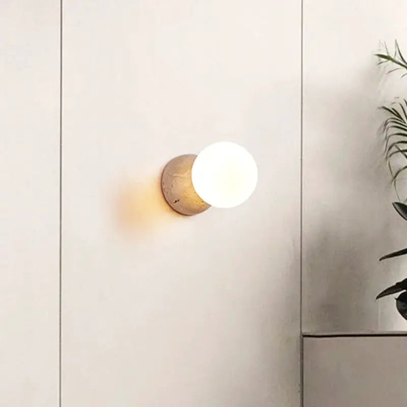 Cream-style LED wall lamp with round white globe and stone base.