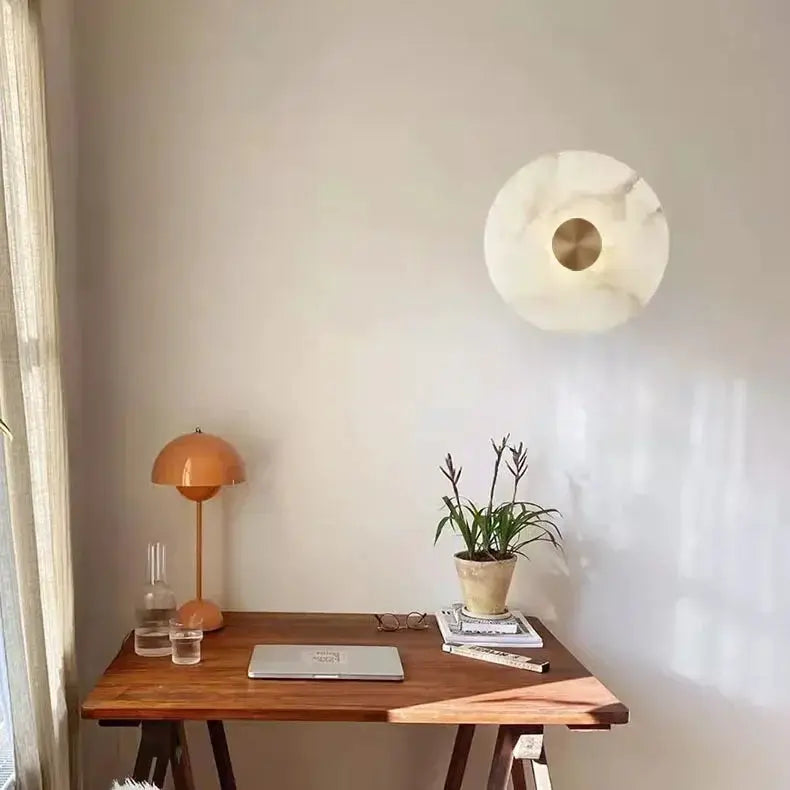 Luxury Spanish natural marble wall lamp with copper center on wall above a wooden desk, paired with an orange desk lamp