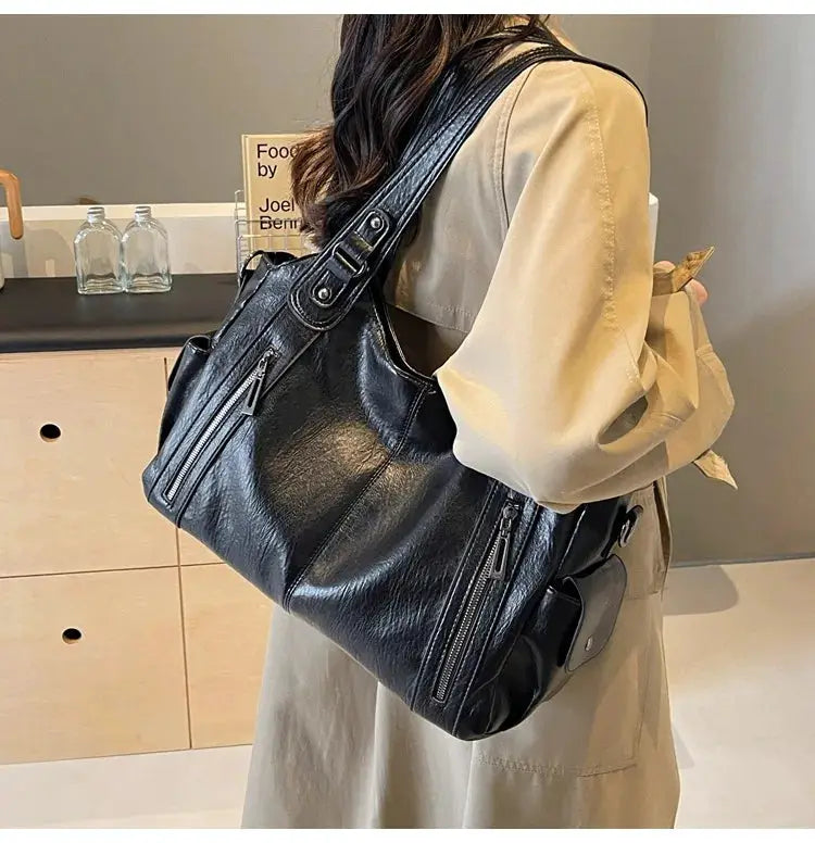 Soft interior compartment shoulder bag in black PU leather with multiple zip pockets.