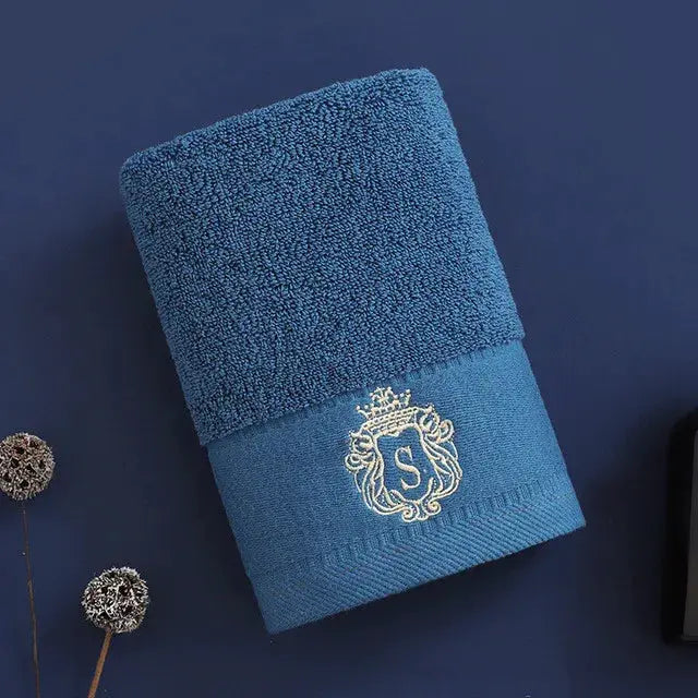 Blue cotton towel with embroidered crest logo featuring S, folded for display