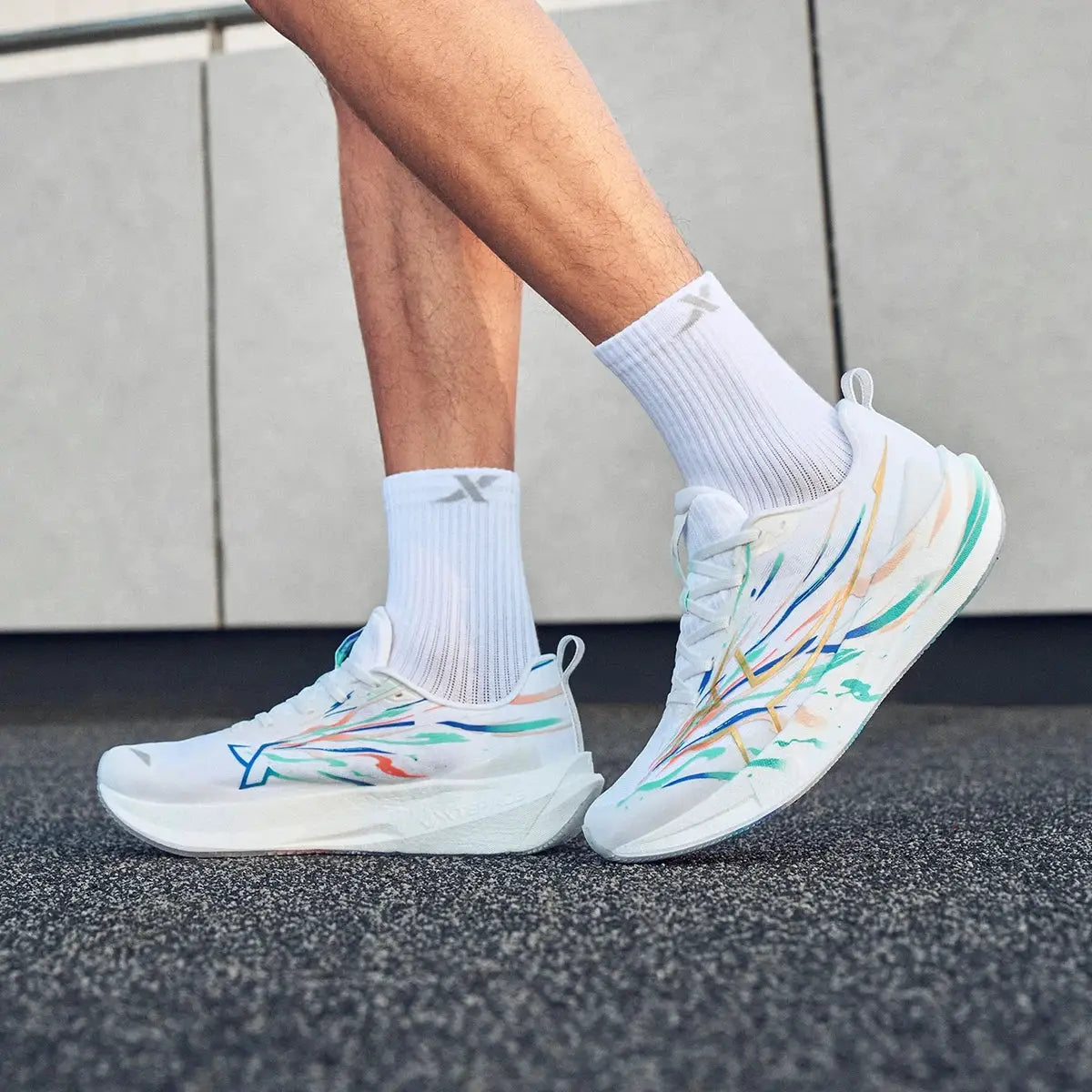 White running shoes with colorful abstract strokes and a chunky cushioned sole, worn with white socks.