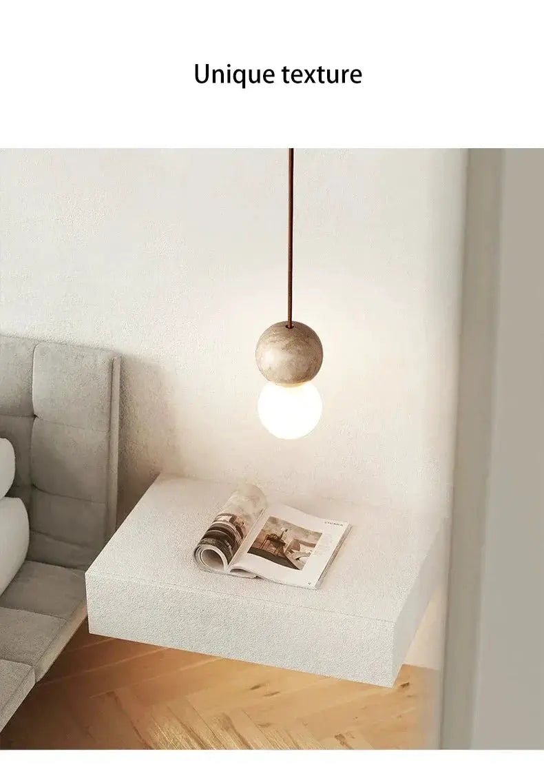 Led pendant light Stone Cream by Simples Market; round stone orb with white bulb over a modern bedside table.