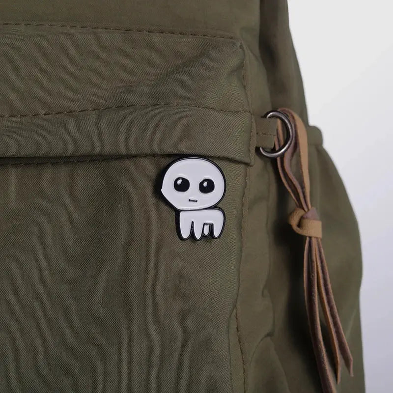 Autism Awareness enamel pin on olive backpack; white cartoon character with black eyes.