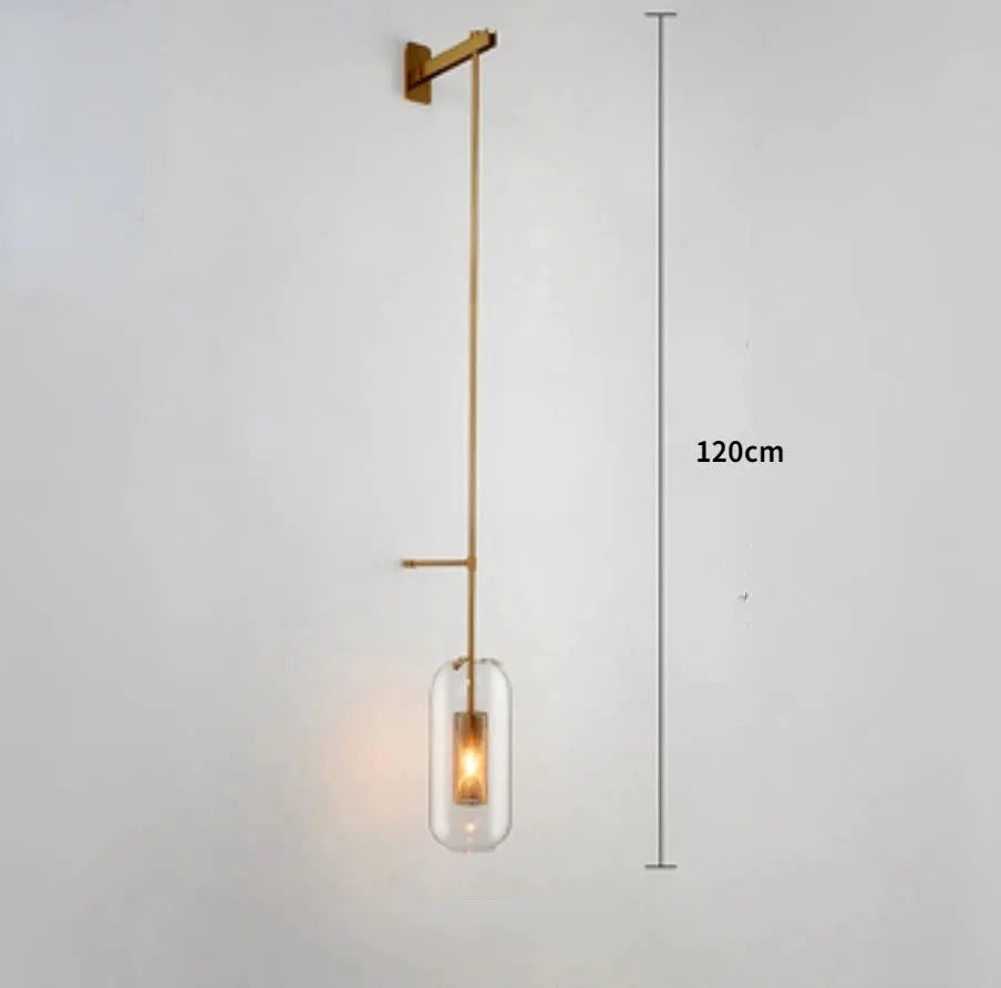 Modern glass wall light sconce with brass vertical frame and clear glass cylinder shade housing an LED filament bulb