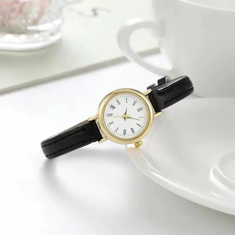 Women’s quartz watch with black leather strap and gold-tone case, white dial with Roman numerals.