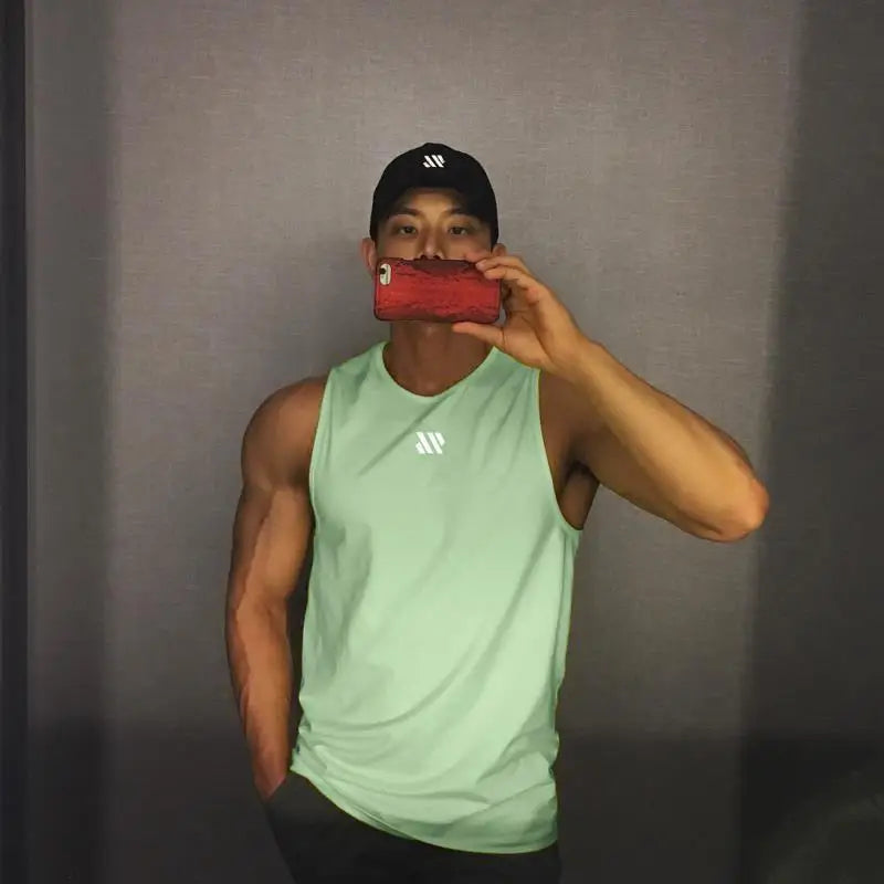 Men's mint green sleeveless gym tank top by Simples Market, shown in a mirror selfie with a black cap and a chest logo