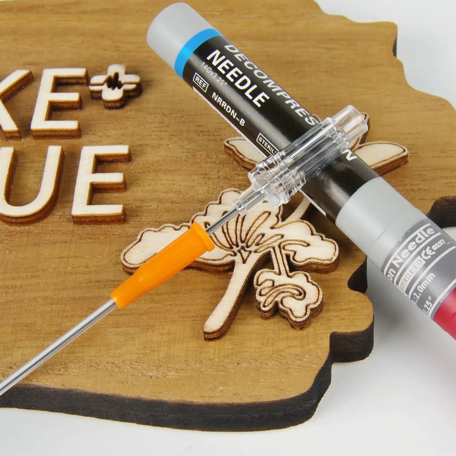 Simples Market needle decompression kit with orange safety cap and clear hub, displayed on a wooden surface