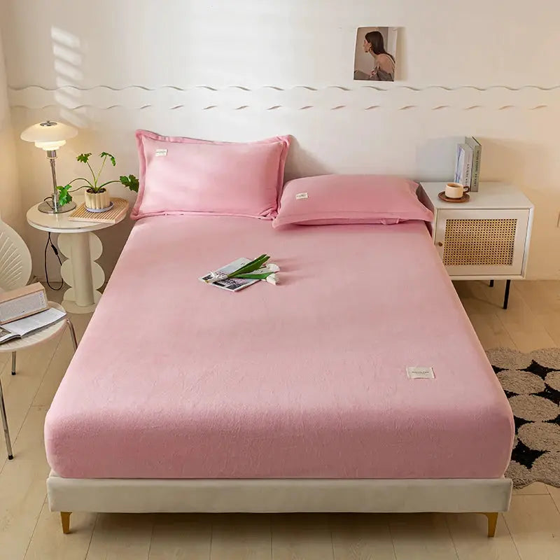 Velvet thermal mattress cover in pink with plush fabric on a bed with matching sheets and pillows.