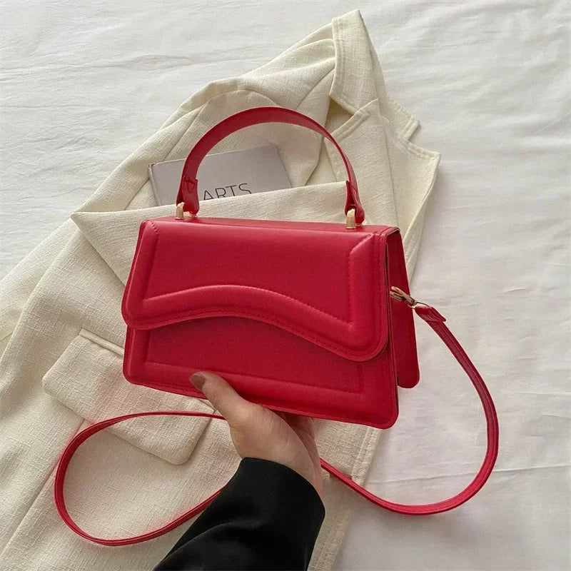 Red PU leather handbag with curved flap, top handle, and long shoulder strap